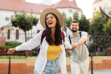 Heyecanlı bir çift el ele tutuşup gülüyor, şehir merkezinde yürüyor, gülen genç bayana odaklanıyor.