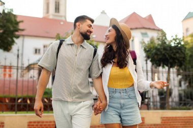 Şehirde yürürken el ele tutuşup birbirlerine bakan mutlu Avrupalı turistler.