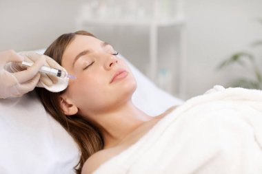 Güzel bayan estetik iyileştirme tedavisi görüyor ve gençlik iğnesi oluyor. Kozmetikçi kusursuz yüz için iğne yapıyor.