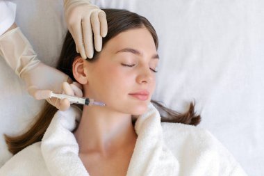 Kozmetik uzmanı çene kaldırma prosedürünü uyguluyor, genç bayana güzellik aşıları yapıyor, yüz gençleştirme tedavisi, üst görüş.