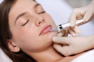 Dudak büyütme için enjeksiyon prosedürü. Kozmetik uzmanı yavaşça ve dikkatlice kadının dudaklarına dolgu yapıyor.