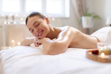 Spa salonunda uzanıp aromaterapi ve atmosferin tadını çıkaran mutlu ve rahat bir bayan masaj seansını bekliyor. Vücut masajı konsepti