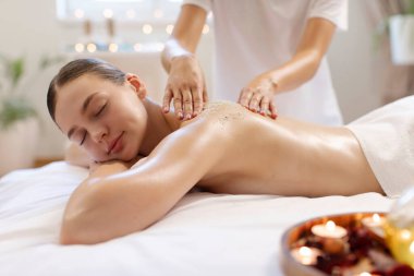 Masör elleri bayanların sırtına deniz tuzu sürüyor, kadın modern kaplıcada, huzurlu atmosferde tuz masajı yaptırıyor.