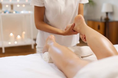 Spa salonunda ayak ve bacak masajı yaptıran bir bayan müşteri, profesyonel masör, genç bayanın ayağını yoğuran, mumlarla dolu sakin bir atmosfer.