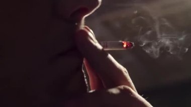 Çok yakın çekim, adam sigara yaktı, dudaklarını yaladı ve karanlık odada dumanı serbest bıraktı..