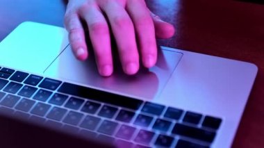 Kırpılmış bir adamın eli, dizüstü bilgisayarda dokunmatik bir zemini manipüle etmek, yüksek açılı görüş, neon mavisi tonlarla aydınlatılmış..