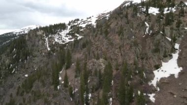 Dağın yamacında kırmızı kayalar, arka planda kar var. 4K 'da drone ile çekiliyor.