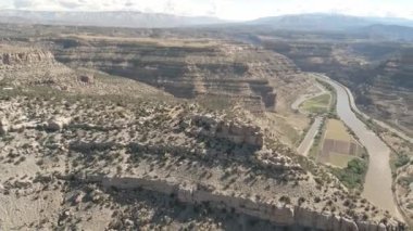Katmanlı kayalarla kaplı kanyon ve aşağıdaki yaşam manzaralı çalılıklar ve küçük çiftçilik