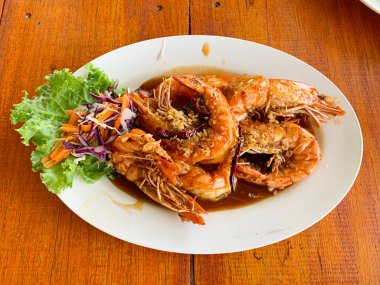 Kahverengi plastik tabakta demirhindi soslu kızarmış karides ve arka planda ahşap.