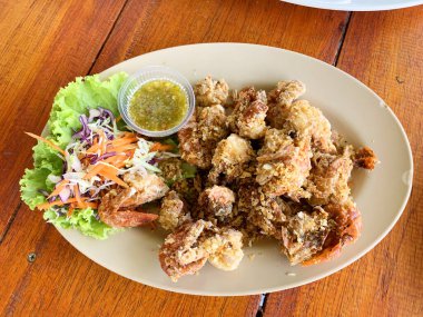 Kızarmış yumuşak kabuklu yengeç, sarımsaklı ve biberli, kahverengi plastik tabakta deniz ürünleri soslu.