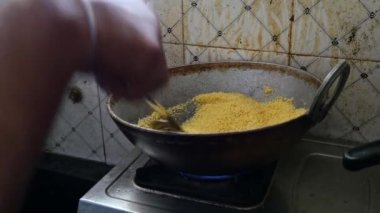 Closeup of male hand roasting Sooji or semolina in a round steel frying pan to prepare dish upma