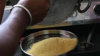 Closeup of roasted sooji or semolina poured into steel plate from steel pan to prepare dish upma