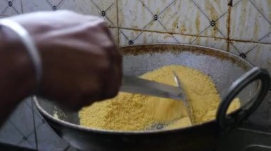 Closeup of male hand roasting Sooji or semolina in a round steel frying pan to prepare dish upma