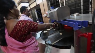 Kaiwara,Chikkaballapura,India-January 5,2017:A woman inspecting grilled bread or chapati on an automatic machine inside the kitchen