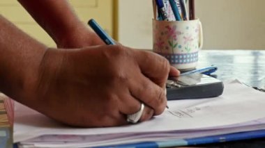 Closeup of calculating with calculator while writing on paper on the wooden table