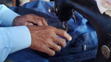 A closeup of an Indian tailor sewing clothes on an old sewing machine inside the shop