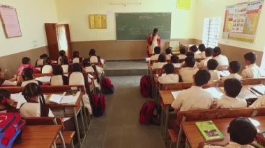 Kaiwara,Chikkaballapura,India-January 6,2017:Back view of students sitting on the benches while the teacher teaches in the classroom at a rural school in Karnataka