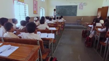 Kaiwara,Chikkaballapura,India-January 6,2017:Back view of students sitting on the benches while the teacher teaches in the classroom at a rural school in Karnataka