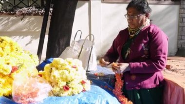 Bangalore,India-February 12,2023:A close-up of a Hindu woman making a red crossandra garland with hands at roadside shop