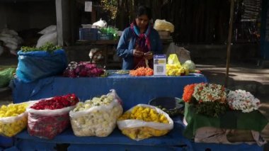 Bangalore,India-February 12,2023:Indian woman making a crossandra and jasmine garland with her hands at a roadside flower shop during sunny day