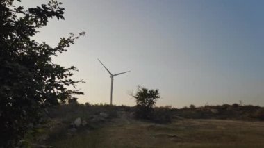 View of a spinning wind turbine on a hill against the sky during sunset at summer