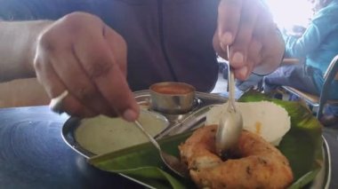 Close up of man eating idly and vada placed over the banyan leaf in plate.South Indian breakfast recipe Idly or Idli rice cake served with coconut chutney and sambar
