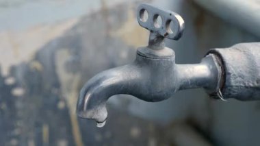 Closeup of the dirty old water tap outside the bathroom, water drops drip from the tap at day time