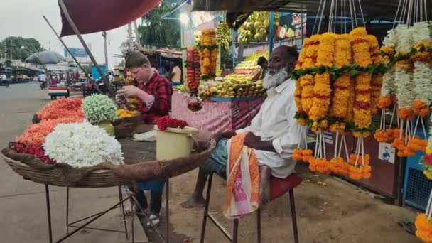 インド ヴィジャヤナガラ2023年4月16日 夏の間 道端の店で座っている老人と幼い子供がガーランドを作っている様子 — ストック動画