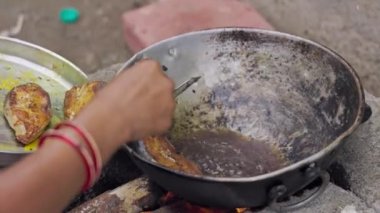 Hintli bir kadın, tuğla ocağın tavasında geleneksel yöntemle balık pişiriyor. Tuğla ocakta odun yakarak yemek pişiriliyor. Ahşap ateş