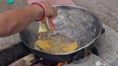 Hintli bir kadın, tuğla ocağın tavasında geleneksel yöntemle balık pişiriyor. Tuğla ocakta odun yakarak yemek pişiriliyor. Ahşap ateş