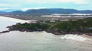 Joaquina Sahili, Atlantik Ormanı ve turkuaz okyanusla kaplı kayalık kıyı şeridini Florianopolis, Santa Catarina, Brezilya 'da ufukta birçok dağ ve kum tepesi görüyordu..