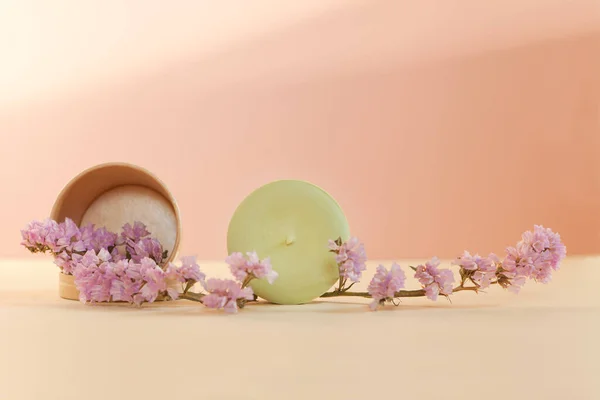 solid shampoo in sunlight with dried pink flowers. Eco friendly handmade bar on light colored background close-up. Hair care from nature. Zero waist without plastic.