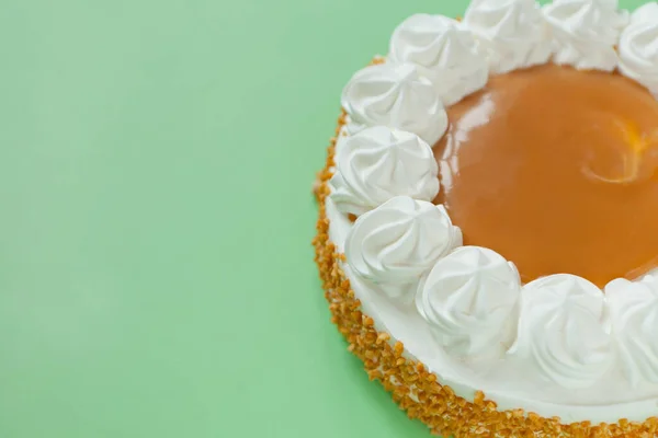 Caramel cake with nuts and caramel sauce glaze. whipped cream on green background, rounded tart or pie