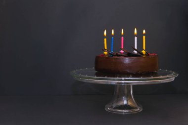 Beş renkli kandeleli çikolatalı pasta. Siyah arkaplanda mum ışığı olan doğum günü pastası
