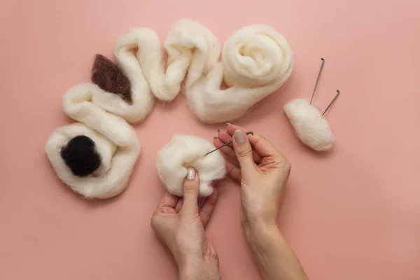 stock image woman hand holding needle felting kit. felted woolen needle and skein of wool on pink table, handicraft from above