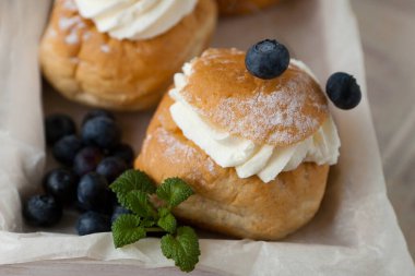 Bir İsveç Semla 'sı, diğer adıyla Shrove bun, badem ezmeli ve krem şantili hafif buğday ekmeği, böğürtlen ve nane içerir. Karton kutu