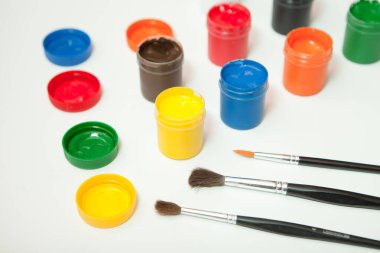 gouache paint with paintbrushes. jars of different colors on white background. hobby painting. workplace for creativity. home teaching concept drawing