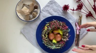 nest with easter eggs on blue plate. Happy Easter. Stylish white table, flat lay. Natural colourful eggs and spring composition from above. High quality 4k footage