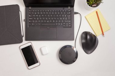 workplace with ergonomic mouse, mobile phone, headphones, column and laptop computer with notebook near tablet. Black devices on white table, designed to reduce injuries such as carpal tunnel syndrome