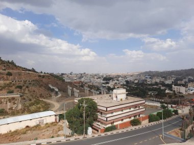 Suudi Arabistan 'daki Al Bahah şehrinin güzel gündüz gökyüzü manzarası. Arka planda şehir binaları, tepeler ve bulutlar görülüyor..