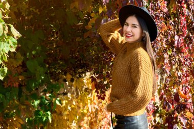 Kahverengi elbiseli ve şapkalı tatlı, rüya gibi genç bayanın seçici odağı. Kırmızı ve sarı yaprakların dallarında dururken sonbaharı düşünüyorum. Yüksek kalite fotoğraf