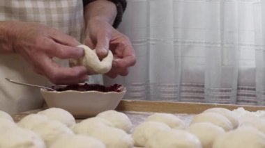 Profesyonel bir mutfakta kıdemli kadın elleri donut yapmak ve içine reçel koymak için un hamuru hazırlıyor. Çiğ hamurun hazırlanması. Ev yapımı donut yapıyorum. Yakın plan. Yüksek kalite 4k görüntü