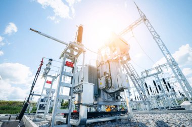 Yüksek voltajlı elektrik hatları ve güneşli bir gökyüzüne karşı donanımlı elektrik santrali, düşük açıyla bakıldığında, bir kablo ve güç dağıtım mekanizması ağı gösteriyor. Güneş, sanayi bölgesini aydınlatıyor..