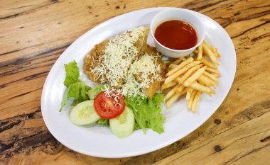 Bir tabak rendelenmiş peynir serpiştirilmiş, sebze, patates kızartması ve sos ile servis edilen tavuk şnitzel.