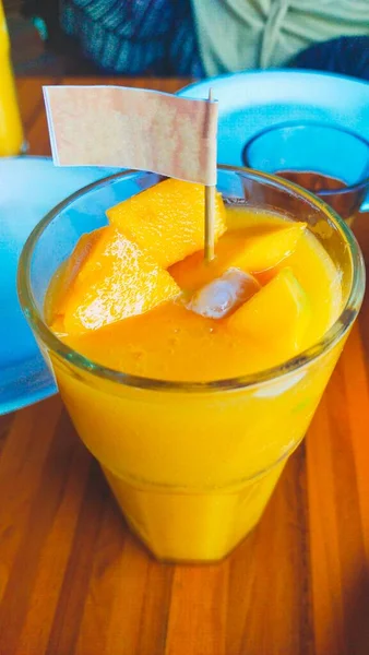 A glass of fresh mango juice with pieces of mango, and flag decoration