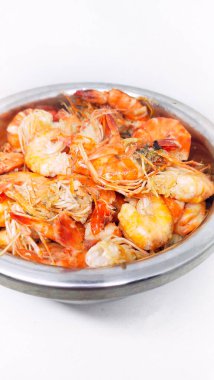 Beyaz arka planda paslanmaz çelikten bir kasede yarı pişmiş karides.