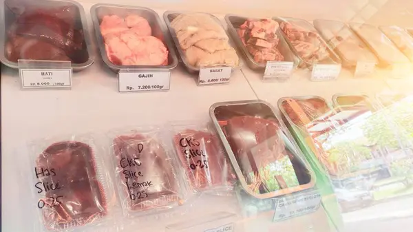 various cuts of raw beef such as thigh, sirloin, ribs, oxtail and others on display in a glass cabinet, sold per 100 grams