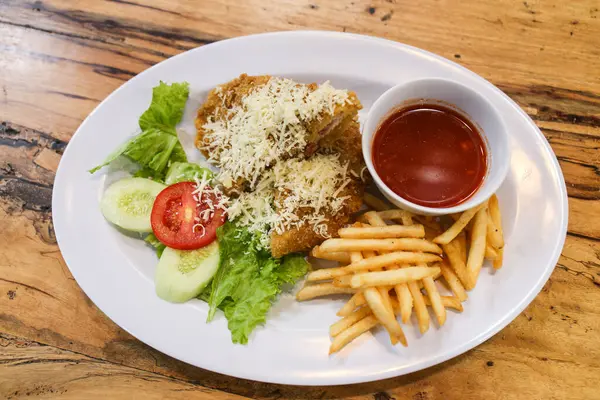 a plate of \'Chicken Schnitzel\' sprinkled with grated cheese, served with vegetables, french fries and gravy
