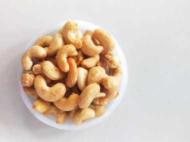 Beyaz arka planda plastik bir kabın içinde kaju fıstığı. Atıştırmalık ya da meze olarak yenebilir.