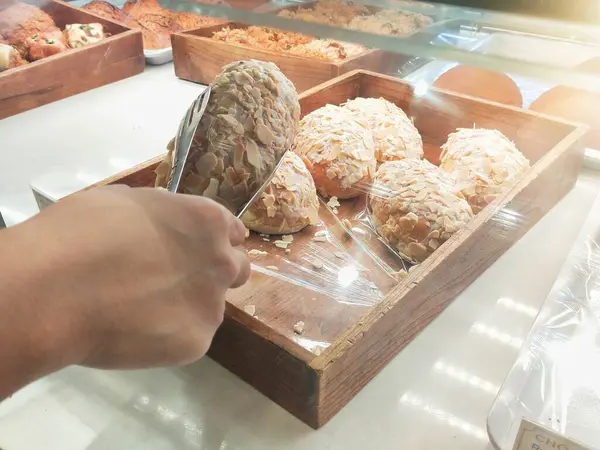 stock image a customer picks up almond bread using tongs from a bakery display case